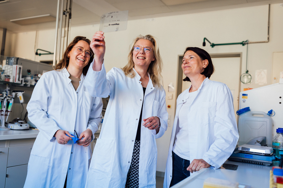 Drei Wissenschaftlerinnen in Kitteln betrachten lächelnd ein Dokument in einem Labor zur LIFE Child-Studie der Universität Leipzig.